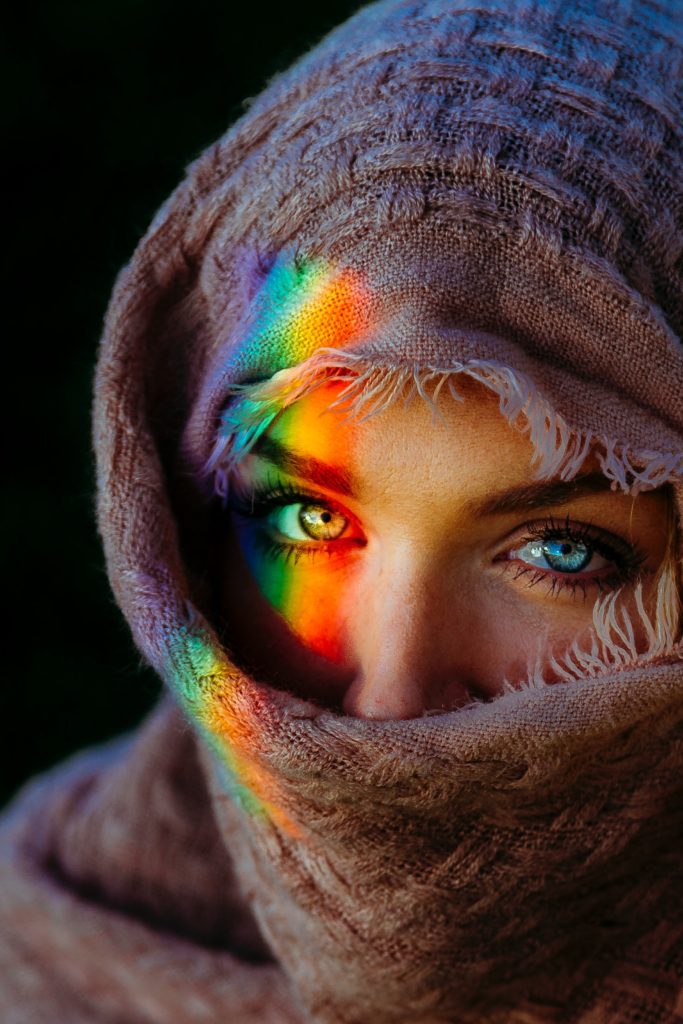 A person with different coloured eyes, head wrapped so only their eyes and nose show, with a a rainbow prism across half their face